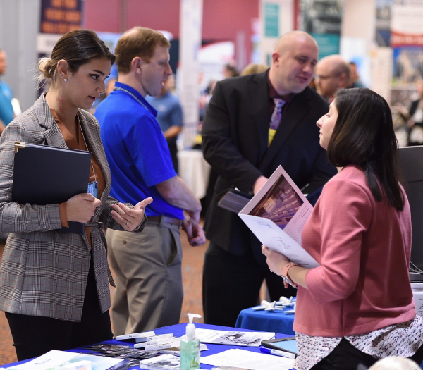 A female student engages in conversation with a woman at a job fair, discussing potential employment opportunities.